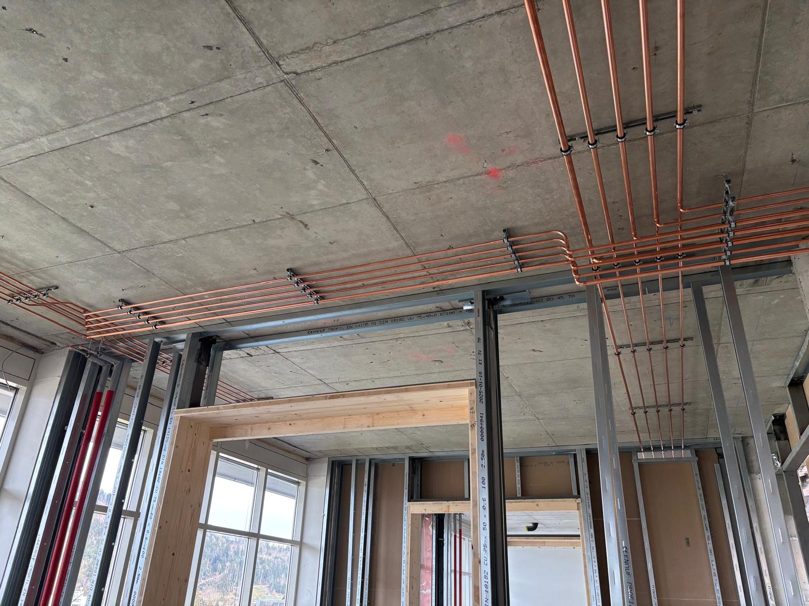 Deckeninstallation eines Medizingas-Verrohrungssystems: parallel geführte Kupferrohre mit Halterungen und Bögen in einem Rohbau-/Technikbereich.